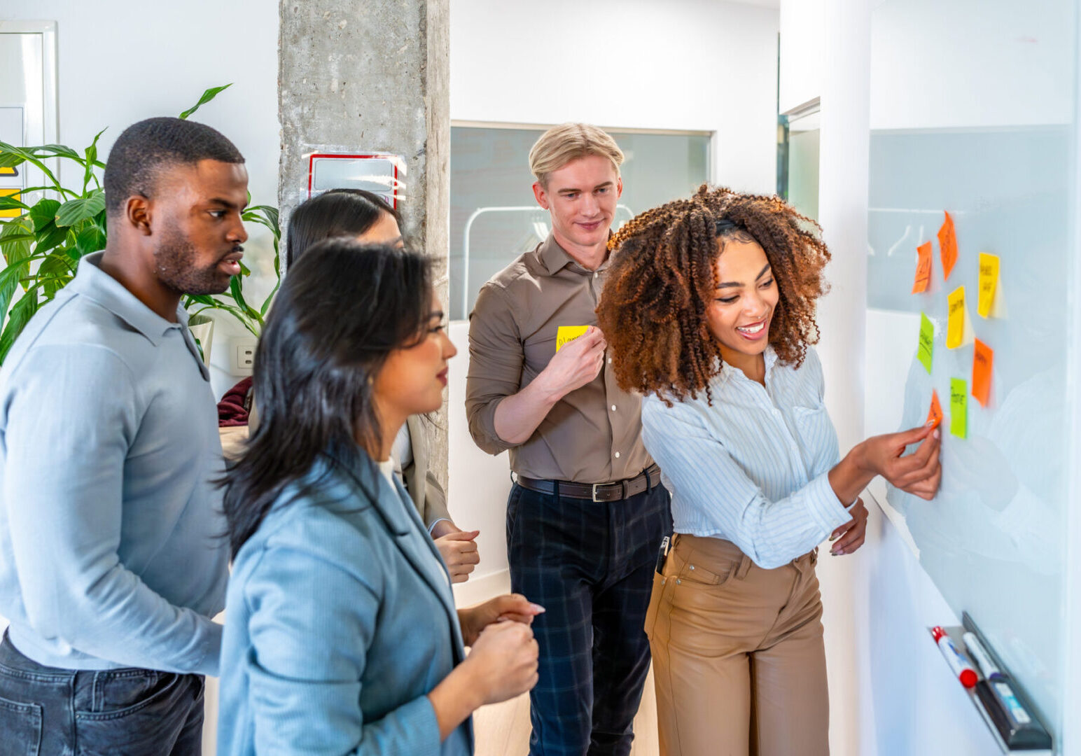 A diverse group discusses ideas around a whiteboard in a bright office.